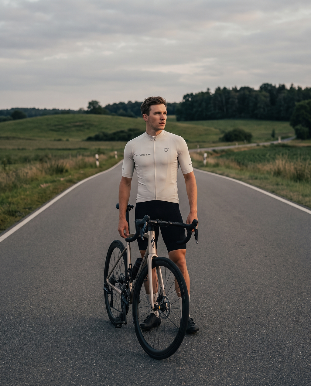 Rennradfahrer im Second Lap Radtrikot neben dem Rennrad auf einer Landstraße